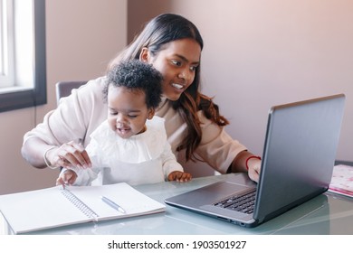 Mixed race Indian mother with African black baby working online from home on Internet. Workplace of freelancer woman with kid. Stay home single mom working distant job. New normal.