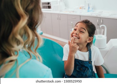 Mixed race little patient showing her perfect toothy smile while sitting dentists chair