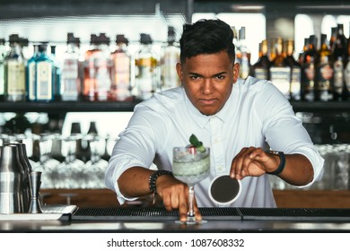 Mixed Race Male Expert Bartender Is Looking At The Camera Presenting A Cocktail And Holding A Coaster At The Bar Counter