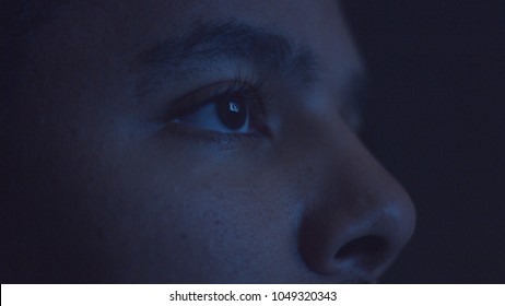 Mixed Race Man Watching Tv In Darkness With Different Color Light From Tv On Face. Eyes Closeup