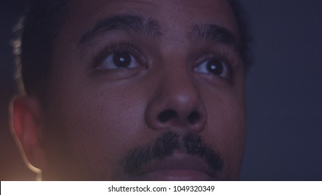 Mixed Race Man Watching Tv In Darkness With Different Color Light From Tv On Face. Eyes Closeup