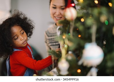 Mixed Race Mother And Daughter Decorating Christmas Tree