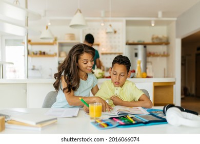 Mixed Race Mother Is Helping Her Son To Finish His Homework. Son Is Listening To His Mother And Writing Down The Answers.