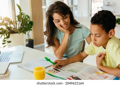 Mixed Race Mother Is Helping Her Son To Finish His Homework. Son Is Listening To His Mother And Writing Down The Answers.