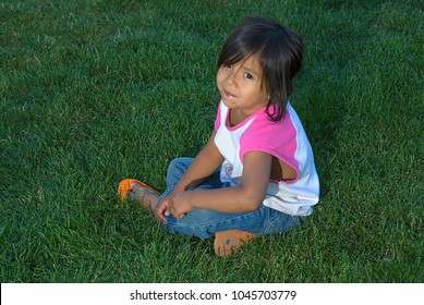 Mixed Race Native-American Latina Girl, Sad, Looking Up At Camera, Sitting In The Grass. Brown Eyes, Brown Hair, 5-year-old Hispanic / Indian Girl