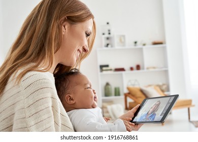 Mixed Race Parent And Child, Young Caucasian Mother Holding Cute Crying African Infant Baby Daughter Looking At Tablet Having Virtual Distance Business Or Family Meeting Video Call Working From Home.