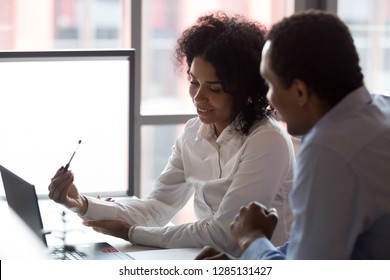 Mixed race pretty millennial businesswoman sitting together with african american business partner, smart people negotiating using computer looking at device screen cogitating making decision concept