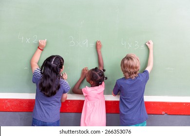 Mixed race school children writing on chalkboard.