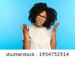 Mixed race shocked female portrait with frowning open mouth, angry surprised face expression on blue background. Young black girl confused with bad news. Casual afro lady with curly hair upset amazed