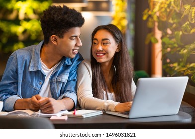 Mixed race student couple sitting in cafe, looking at each other and smiling, copy space