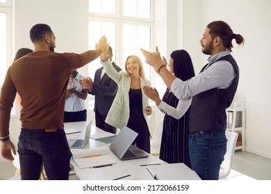 Mixed race team of business people celebrating result of successful teamwork. Happy young woman and man high five each other while coworkers are applauding, with sun lighting up room giving lens flare - Powered by Shutterstock