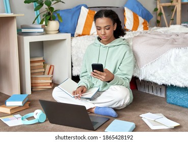 Mixed Race Teen School Girl Distant School Or College Student Virtual Remote E Learning Using Mobile Phone App And Laptop In Bedroom. Distance Education Classes, Studying Online At Home Concept.