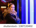 Mixed race teenage with fur coat standing next to window with blue light.