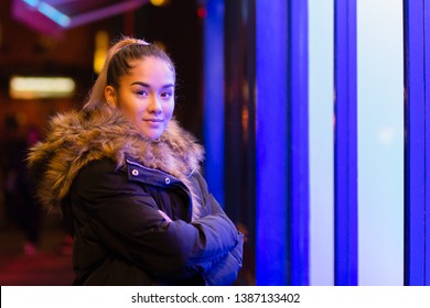 Mixed race teenage with fur coat standing next to window with blue light.