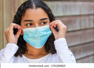 Mixed race teenager teen girl young woman wearing fitting and adjusting a face mask during the Coronavirus COVID-19 pandemic - Powered by Shutterstock