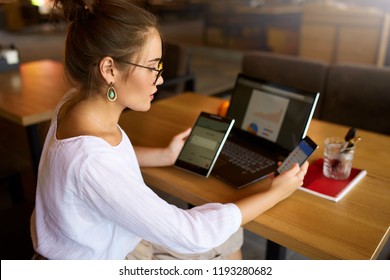 Mixed race woman in glasses working with multiple electronic internet devices. Freelancer businesswoman has tablet and cellphone in hands and laptop on table with charts on screen. Multitasking theme - Shutterstock ID 1193280682