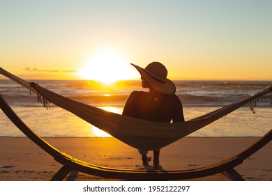 Mixed Race Woman On Beach Holiday Sitting In Hammock During Sunset. Healthy Outdoor Leisure Time By The Sea.