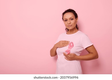 Mixed race woman puts hands around pink ribbon on her pink T Shirt, for breast cancer campaign, supporting Breast Cancer Awareness. Concept of 1 st October Pink Month and women's health care - Shutterstock ID 2037956996