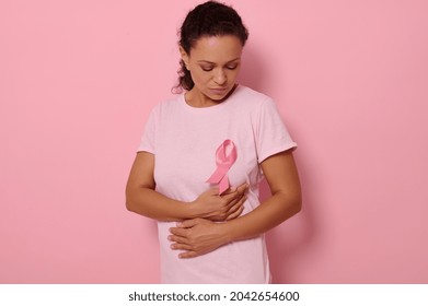 Mixed race woman puts hands under pink ribbon on a pink T Shirt, for breast cancer campaign, supporting Breast Cancer Awareness. Concept of 1 st October Pink Month and women's health care. Copy space