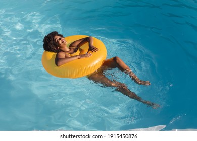 Mixed race woman sunbathing on inflatable in swimming pool. Hanging out and relaxing outdoors in summer.