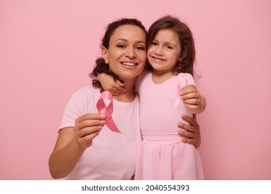 Mixed race young woman hugs her daughter, holding pink ribbon, cute smiles looking at camera, isolated on colored background with copy space. International Day of fight against a Breast Cancer disease - Powered by Shutterstock