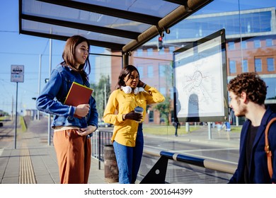 Mixed raced group of three friends millennial students meet together on tram stop. Millennials passengers traveling with public transport concept.