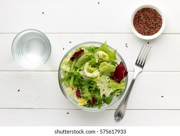 Mixed Salad In Glass Bowl With Flax Seed And Water On White Wooden Table. Top View.