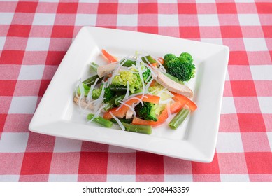 Mixed Salad On White Plate With Mixed Greens, Cucumber, Brocolli, Squash And Carrots Served On Red Plaid Table Cloth. Italian Cuisine Concept. Dinner Idea.