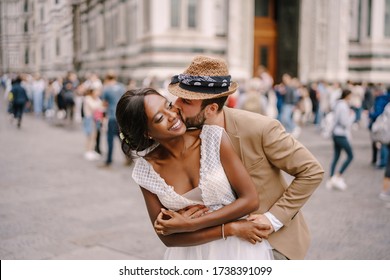 Mixed-race wedding couple. Wedding in Florence, Italy. Caucasian groom hugs from behind and kisses African-American bride. - Powered by Shutterstock