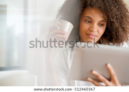 Mixed-race woman at home using tablet and drinking tea