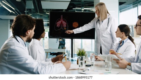 Mixed-races medical team of doctors discussing coronavirus data on digital display showing the virus outbreak and rating. Healthcare workers talking about pulmon infection. Covid-19 pandemic concept - Powered by Shutterstock