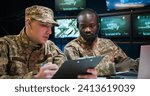 Mixed-races military male workers sitting in monitoring center and studying data from conflict zones. African American man in headset typing on laptop computer while Caucasian soldier reading document