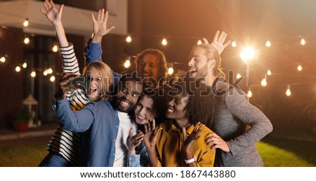 Mixed-races young happy and cheerful friends, men and women smiling and posing to smartphone while taking selfie photo at night. late evening party. Multi ethnic men and women having fun.