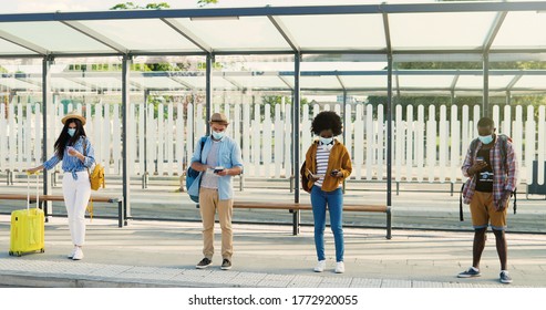 Mixed-races young males and females people im medical masks standing in line at bus stop. Keeping safe social distance. Multiethnic stylish men and women tourists outdoor waiting for transport.
