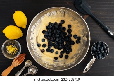 Mixing Bowl Filled with Muffin Batter and Fresh Blueberries: Bowl of blueberry muffin batter surrounded by fresh ingredients and kitchen utensils - Powered by Shutterstock