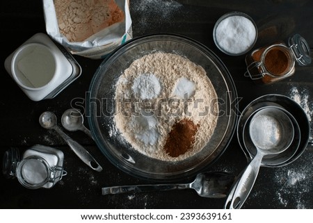 Mixing Dry Ingredients for Baked Apple Cider Donuts: Whole-wheat pastry flour in a glass mixing bowl surrounded by kitchen tools and ingredients