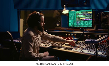 Mixing engineer pressing sliders on control desk to balance tracks and add sound effects, creating new music. Audio engineering expert works with motorized faders in professional studio. Camera B. - Powered by Shutterstock