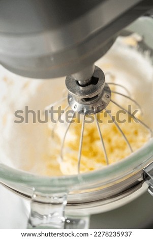 Mixing ingredients in a large glass mixing bowl of kitchen mixer to make eggnog buttercream frosting.