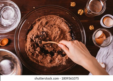Mixing melted chocolate and cocoa powder in large bowl to make dough for delicious brownie cake on dark wooden table