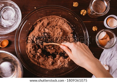 Mixing melted chocolate and cocoa powder in large bowl to make dough for delicious brownie cake on dark wooden table