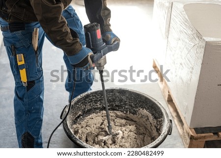 Mixing mortar using a handheld material mixer in the mortar bin.