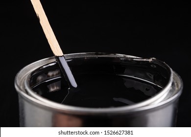 Mixing paint with a wooden stick in a metal can. Preparation of a black emulsion for painting. Dark background.