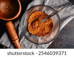 Mixing Spices to make Berbere Spice Blend: Ground herbs and spices mixed with a spoon in a glass bowl next to a wooden mortar and pestle