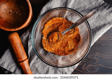 Mixing Spices to make Berbere Spice Blend: Ground herbs and spices mixed with a spoon in a glass bowl next to a wooden mortar and pestle - Powered by Shutterstock