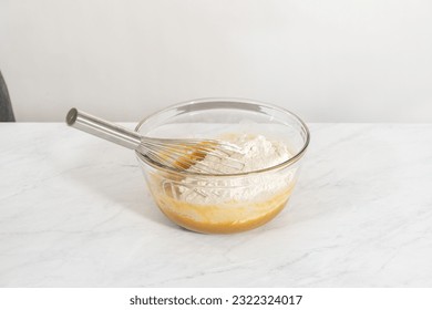 Mixing wet and dry ingredients with a hand whisk in a glass mixing bowl to bake white chocolate macadamia nut. - Powered by Shutterstock