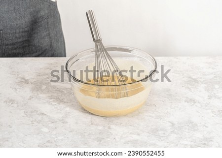Mixing wet and dry ingredients with a hand whisk in a glass mixing bowl to bake a carrot bundt cake with cream cheese frosting.