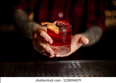 Mixologist Holding A Glass Of Strong Fresh Whiskey Cocktail Decorated With Orange Peel On The Bar