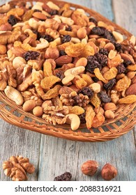 A mixture of nuts and raisins, in a wicker basket on a wooden table.                              