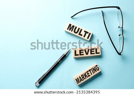 MLM - multi level marketing text on a wooden block ,blue background