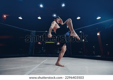 MMA Training of fighter without rules in octagon cage kick in flight on dark background.
